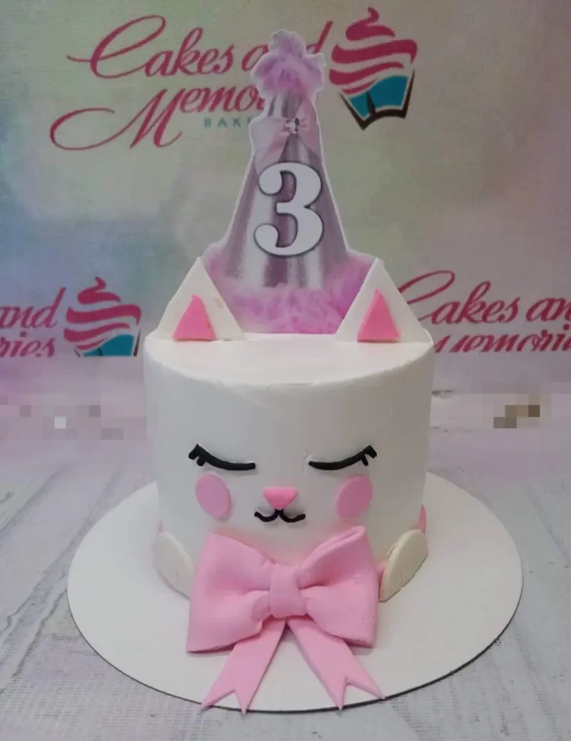 White cat-themed birthday cake with pink fondant bow, ears, and a purple party hat printout topper. White cat-themed birthday cake with pink fondant bow, ears, and a purple party hat printout topper.