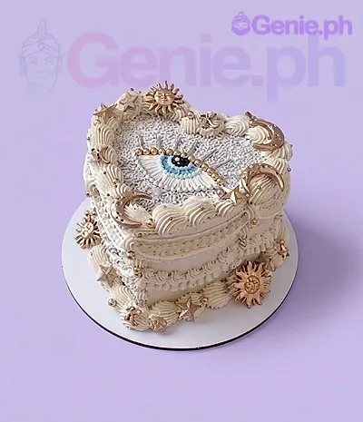 A ivory heart-shaped 1-tier cake themed Celestial Heart, featuring a central eye, gold suns, moons, and ruffles. A ivory heart-shaped 1-tier cake themed Celestial Heart, featuring a central eye, gold suns, moons, and ruffles.