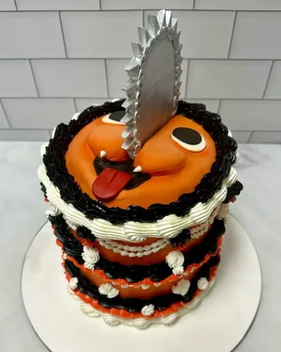 Orange fondant cake with a silver chainsaw blade topper, black and white piped icing borders, and character face details Orange fondant cake with a silver chainsaw blade topper, black and white piped icing borders, and character face details