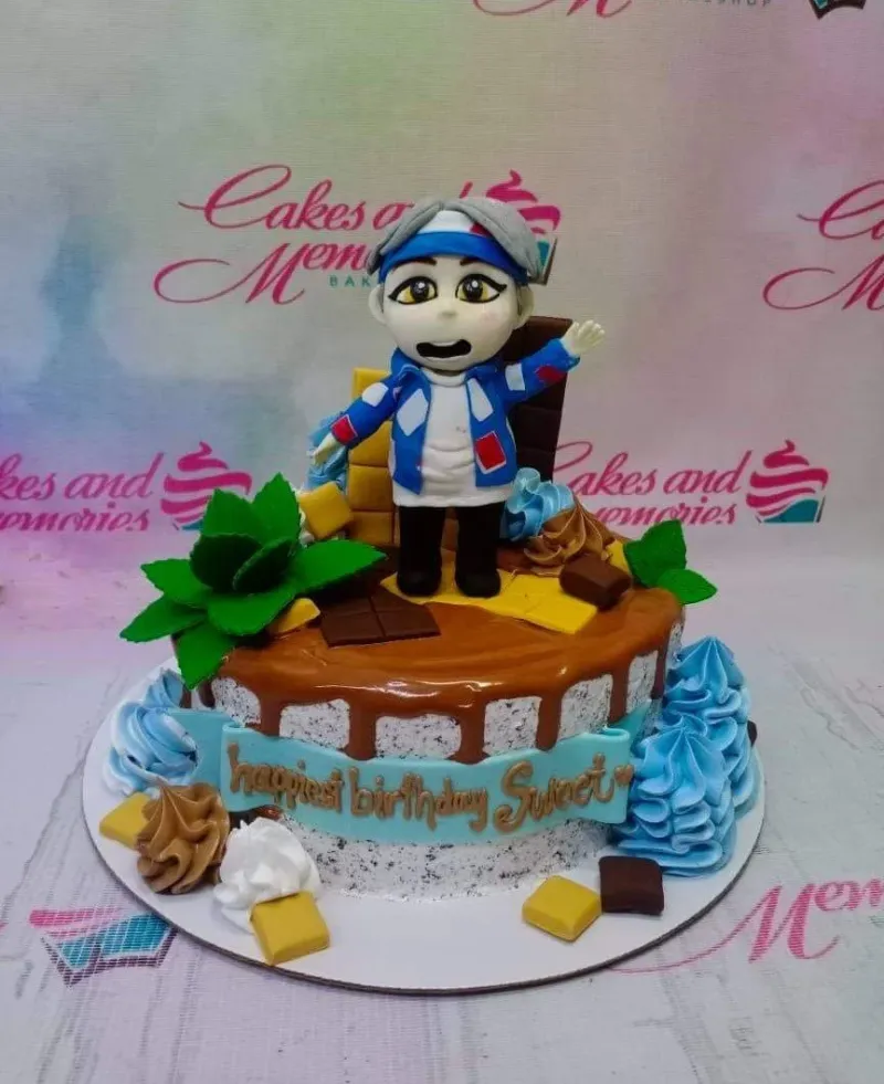 A single-tier cake with white and black speckled icing, a chocolate drip, and a 3D fondant character topper with chocolate bar accents. A single-tier cake with white and black speckled icing, a chocolate drip, and a 3D fondant character topper with chocolate bar accents.