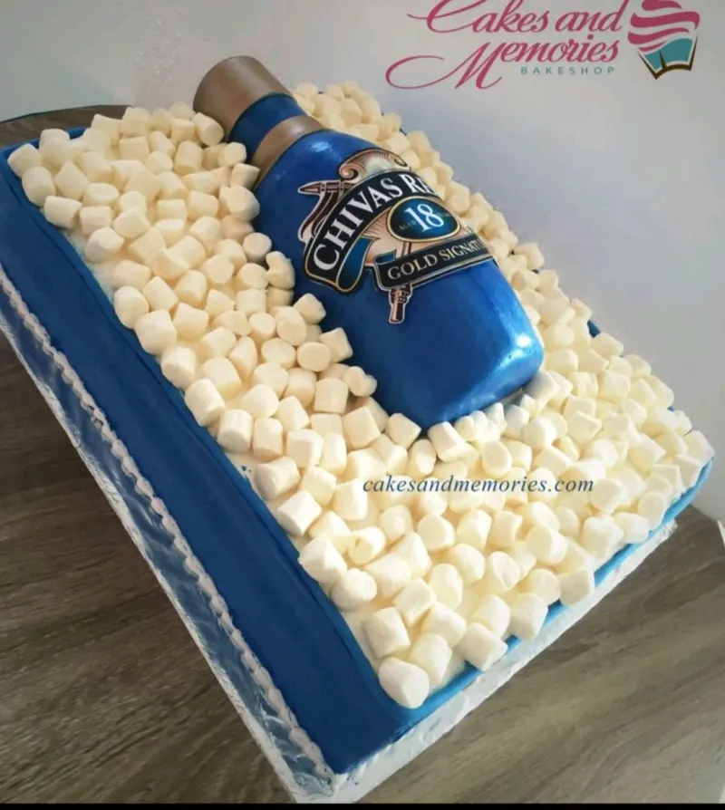 A blue and white rectangular Chivas Regal cake with a blue whiskey bottle, white marshmallows, and a white piped border. A blue and white rectangular Chivas Regal cake with a blue whiskey bottle, white marshmallows, and a white piped border.