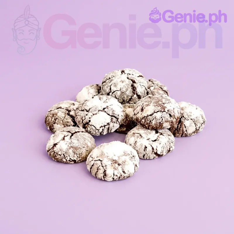 Chocolate crinkle cookies dusted with powdered sugar on a glass cake stand with a wooden spoon. Chocolate crinkle cookies dusted with powdered sugar on a glass cake stand with a wooden spoon.