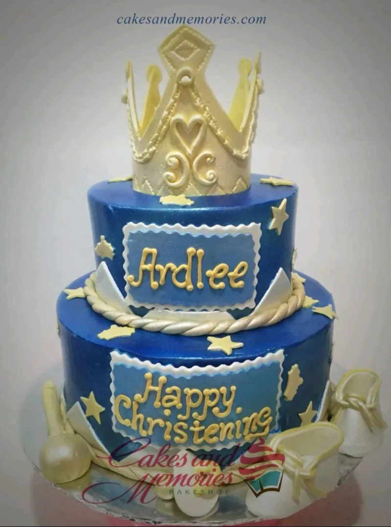 Two-tier royal blue fondant cake with a large gold crown topper, white baby shoes, and gold stars for a christening. Two-tier royal blue fondant cake with a large gold crown topper, white baby shoes, and gold stars for a christening.