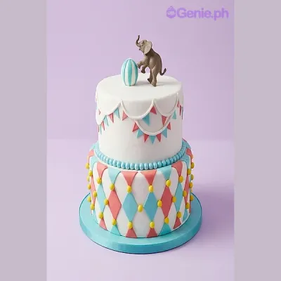 White 2-tier circus themed cake with a sculpted elephant and ball topper and colorful diamond pattern White 2-tier circus themed cake with a sculpted elephant and ball topper and colorful diamond pattern