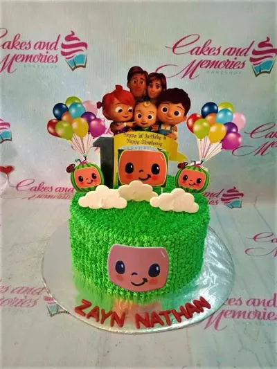 Green Cocomelon themed birthday cake with character printouts, white clouds, and red name letters on the base board. Green Cocomelon themed birthday cake with character printouts, white clouds, and red name letters on the base board.