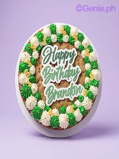A round cookie cake with green and white icing rosettes, gold accents, and a 'Happy Birthday Brandon' topper. A round cookie cake with green and white icing rosettes, gold accents, and a 'Happy Birthday Brandon' topper.