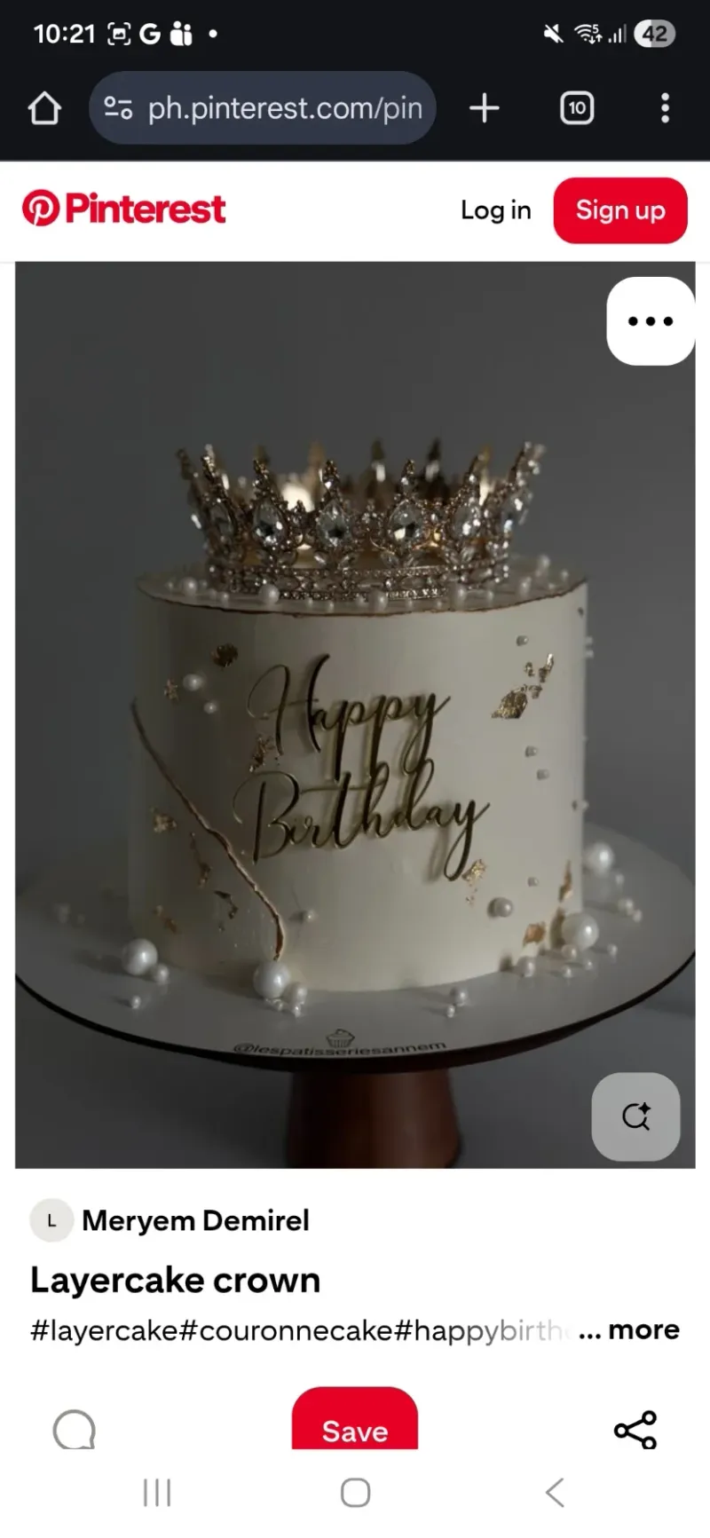 A white 1-tier cake with a crown theme, featuring a large gold crown topper, gold leaf accents, and white pearls. A white 1-tier cake with a crown theme, featuring a large gold crown topper, gold leaf accents, and white pearls.