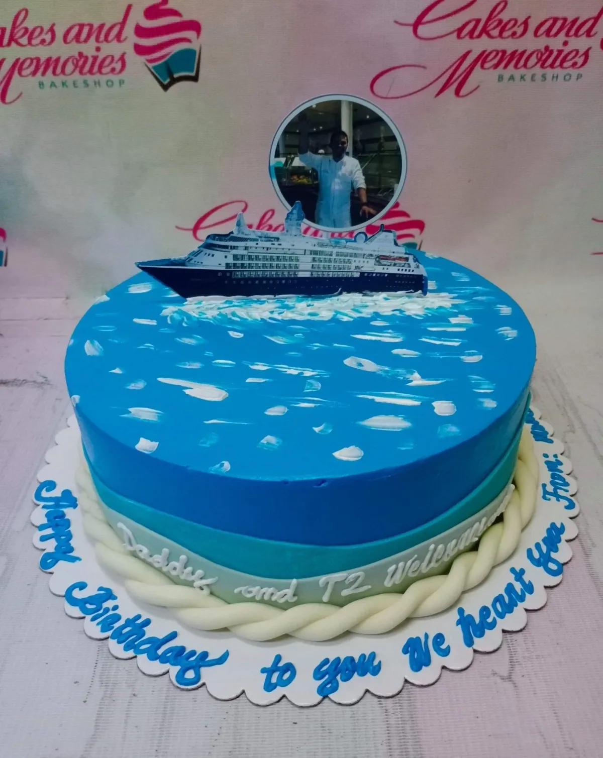 A blue ocean-themed 1-tier cake with a cruise ship printout, a circular photo topper, white icing waves, and a white fondant rope border. A blue ocean-themed 1-tier cake with a cruise ship printout, a circular photo topper, white icing waves, and a white fondant rope border.