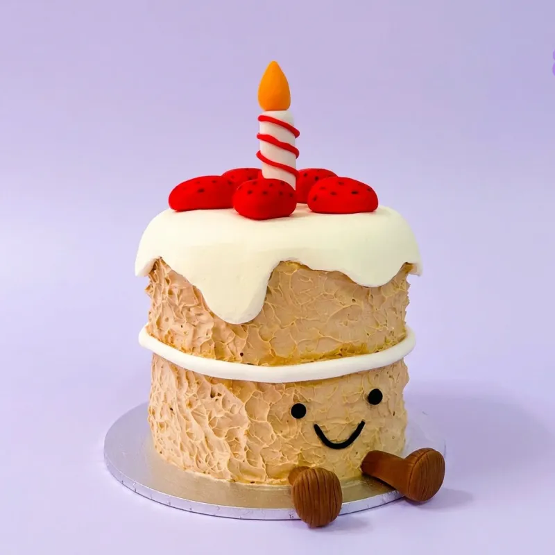 Tan single-tier cake with a cute face, red strawberry toppers, and a candle Tan single-tier cake with a cute face, red strawberry toppers, and a candle