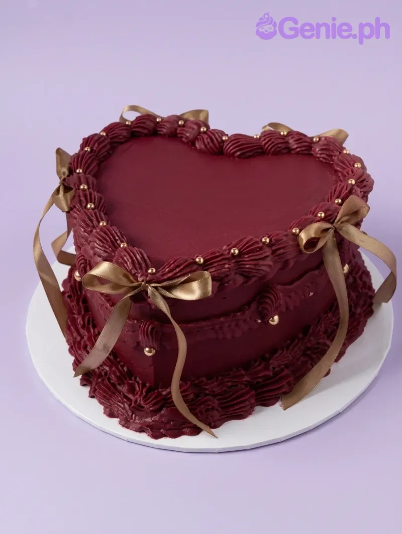 A dark red heart-shaped 1-tier vintage cake with piped ruffles, gold satin bows, and silver dragees. A dark red heart-shaped 1-tier vintage cake with piped ruffles, gold satin bows, and silver dragees.