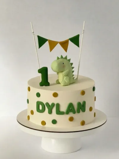 Ivory 1-tier dinosaur cake with soft icing, a pale green dinosaur figure, and gold polka dots Ivory 1-tier dinosaur cake with soft icing, a pale green dinosaur figure, and gold polka dots
