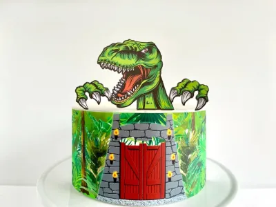 A white, green, and red 1 Tier cake themed around Dinosaurs, featuring a large green T-Rex printout topper and a jungle gate wrap. A white, green, and red 1 Tier cake themed around Dinosaurs, featuring a large green T-Rex printout topper and a jungle gate wrap.