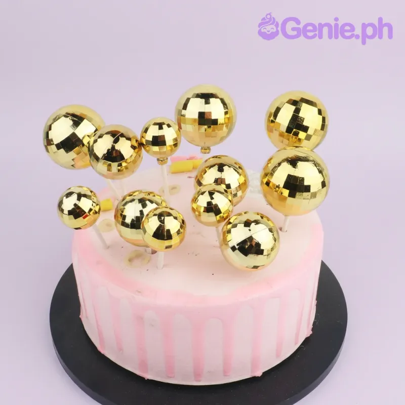 One tier cake with pink icing, pink drip, gold reflective spheres, and small peach fondant shapes One tier cake with pink icing, pink drip, gold reflective spheres, and small peach fondant shapes