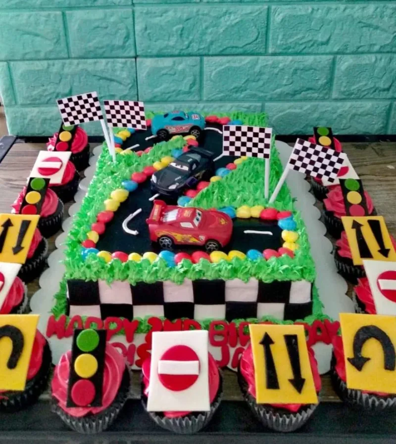 Rectangle racing car themed cake with Lightning McQueen and friends on a black track with green grass icing and checkered borders. Rectangle racing car themed cake with Lightning McQueen and friends on a black track with green grass icing and checkered borders.