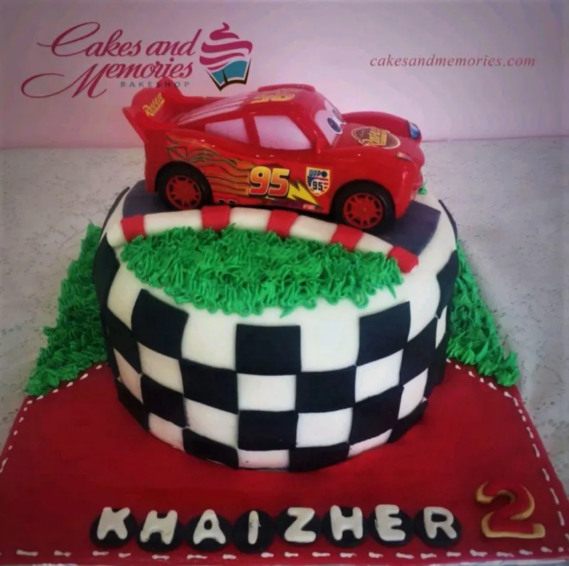 Disney Cars Lightning McQueen themed birthday cake with checkered flag pattern and green grass icing details. Disney Cars Lightning McQueen themed birthday cake with checkered flag pattern and green grass icing details.