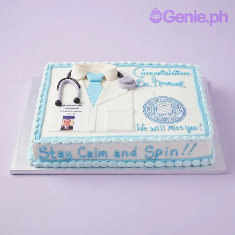 White rectangular soft icing cake with doctor coat decorations, stethoscope, photo ID, and blue piped messages White rectangular soft icing cake with doctor coat decorations, stethoscope, photo ID, and blue piped messages