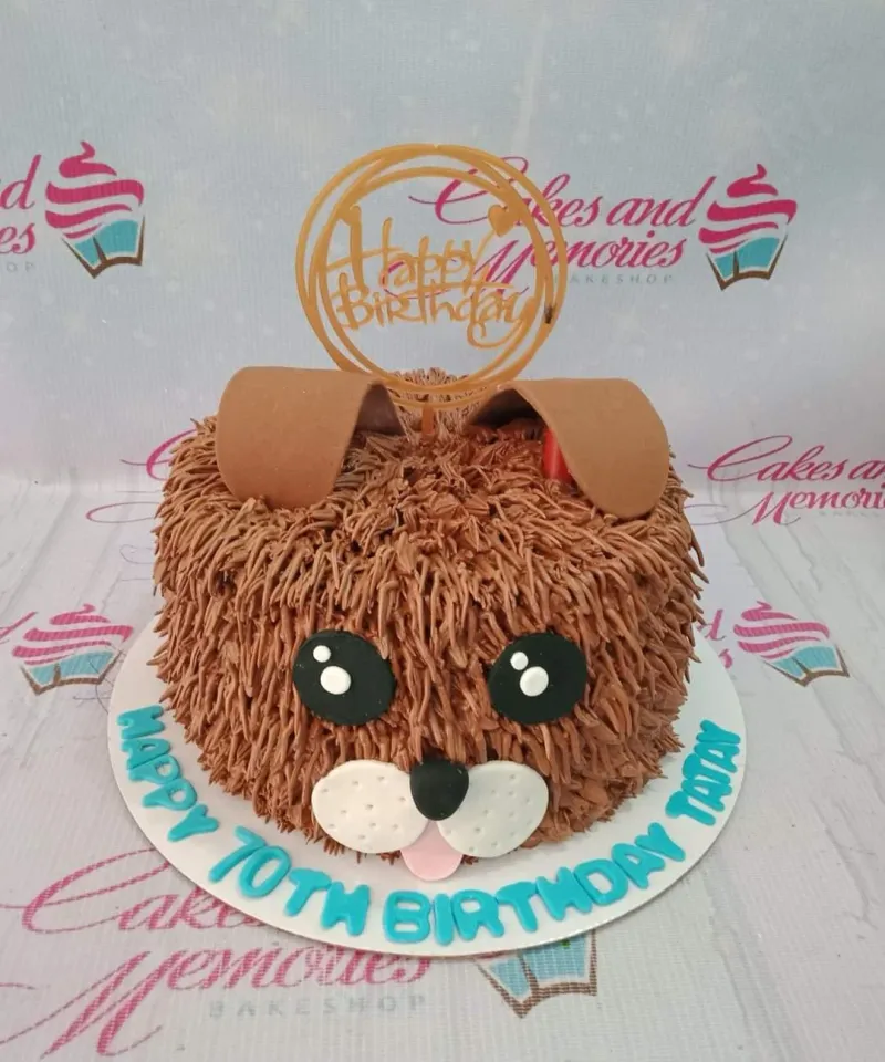 A brown 1-tier cake themed as a shaggy dog, featuring floppy ears, large eyes, and a blue birthday message on a white base board. A brown 1-tier cake themed as a shaggy dog, featuring floppy ears, large eyes, and a blue birthday message on a white base board.