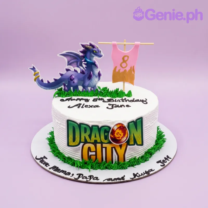 A white 1-tier Dragon City cake, featuring a purple dragon, a pink jersey printout, and green icing grass borders. A white 1-tier Dragon City cake, featuring a purple dragon, a pink jersey printout, and green icing grass borders.