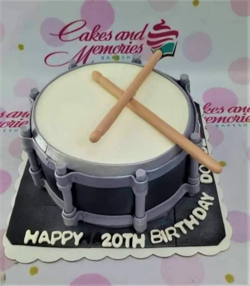 A white, grey, and black 1 Tier Fondant cake, drum-themed, featuring two tan drumsticks and 'HAPPY 20TH BIRTHDAY' text. A white, grey, and black 1 Tier Fondant cake, drum-themed, featuring two tan drumsticks and 'HAPPY 20TH BIRTHDAY' text.