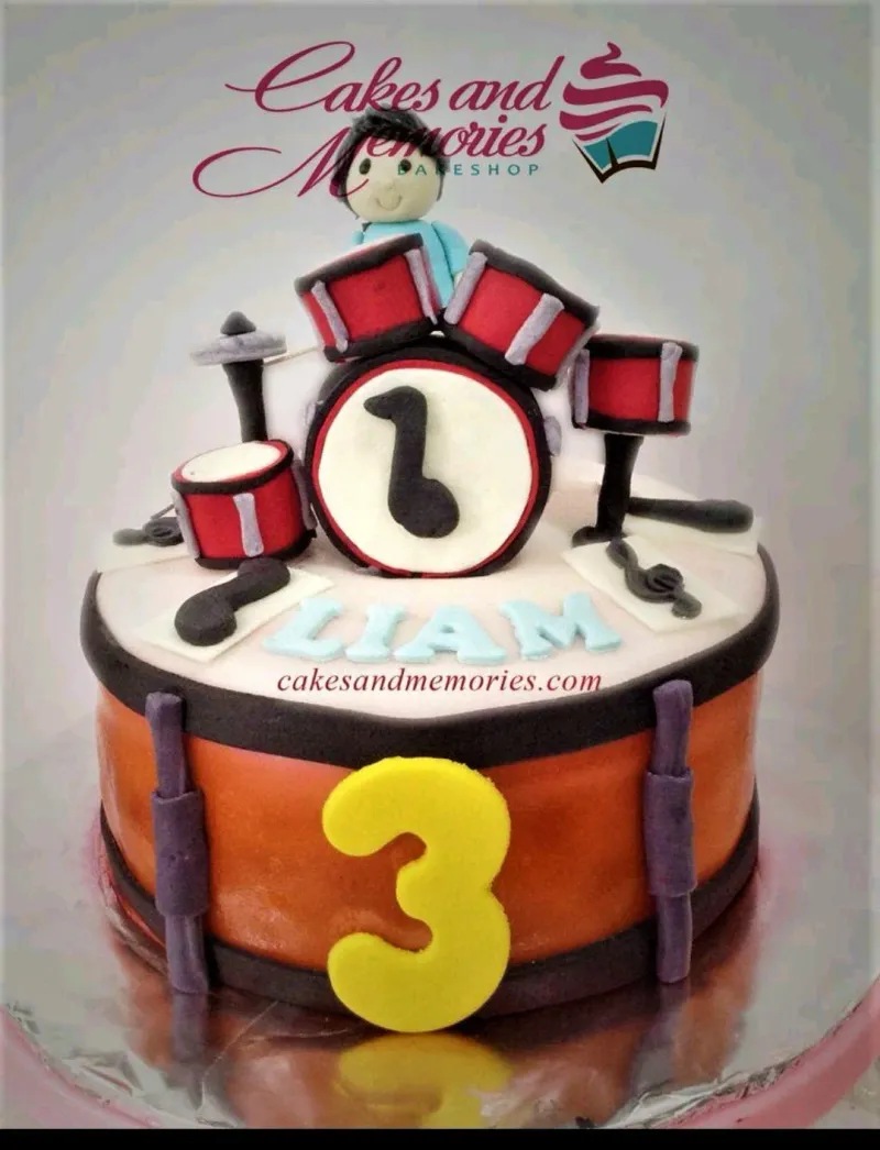 A multicolored 1 Tier Fondant cake themed Drum Set, featuring a drummer boy figure, a red and black drum set, and musical notes. A multicolored 1 Tier Fondant cake themed Drum Set, featuring a drummer boy figure, a red and black drum set, and musical notes.