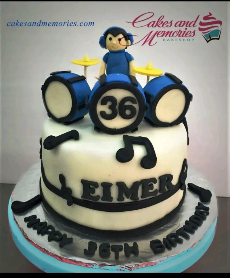 A white, blue, black Fondant drummer cake, featuring a drummer and drum set with musical notes. A white, blue, black Fondant drummer cake, featuring a drummer and drum set with musical notes.