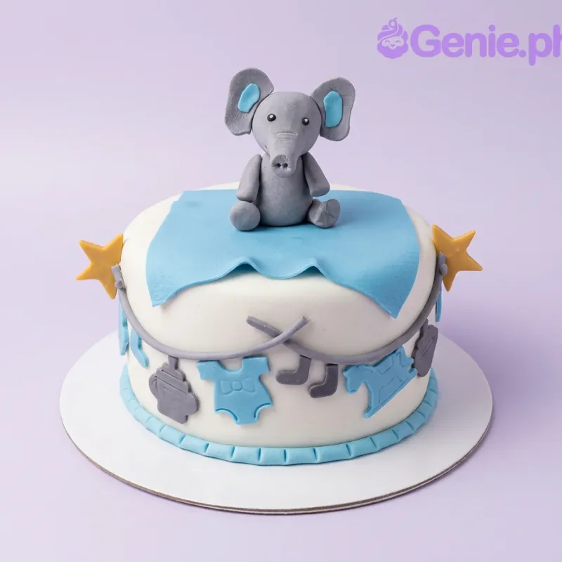 A white 1-tier fondant cake with an Elephant Baby Shower theme, featuring a grey elephant topper, blue blanket, and baby-themed accents. A white 1-tier fondant cake with an Elephant Baby Shower theme, featuring a grey elephant topper, blue blanket, and baby-themed accents.
