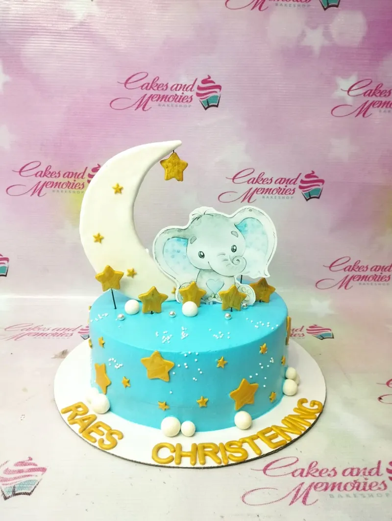 Light blue christening cake with a large white crescent moon, a cute elephant printout, and gold stars. Light blue christening cake with a large white crescent moon, a cute elephant printout, and gold stars.