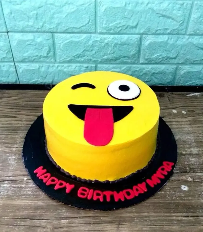 A yellow 1 Tier cake themed around Emoji, featuring a winking emoji face with tongue, pink text on a black board, and black dots. A yellow 1 Tier cake themed around Emoji, featuring a winking emoji face with tongue, pink text on a black board, and black dots.