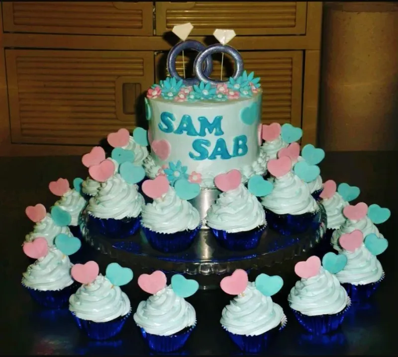 Light blue single tier cake with blue and pink heart toppers and matching cupcakes on a glass stand. Light blue single tier cake with blue and pink heart toppers and matching cupcakes on a glass stand.