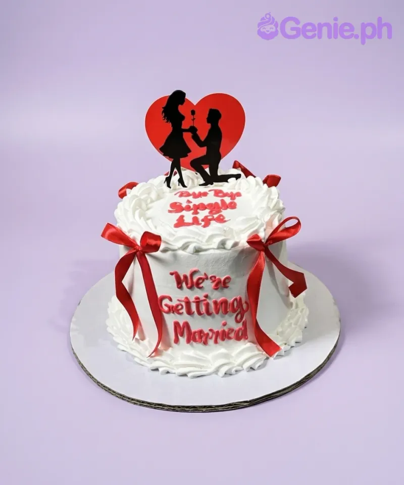 A white 1-Tier Engagement cake, featuring a couple proposing silhouette against a red heart, red ribbon bows, and red text. A white 1-Tier Engagement cake, featuring a couple proposing silhouette against a red heart, red ribbon bows, and red text.