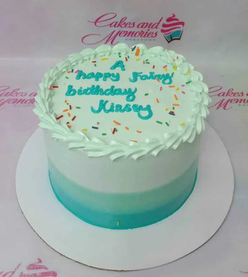 A white and teal gradient 1-tier Fairy Birthday cake, with colorful sprinkles, white piped rosettes, and a teal message. A white and teal gradient 1-tier Fairy Birthday cake, with colorful sprinkles, white piped rosettes, and a teal message.