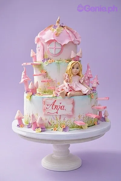 A pink and white 3-tier Fairy House fondant cake, featuring a fondant girl figurine, a mushroom house, mushrooms, and floral accents. A pink and white 3-tier Fairy House fondant cake, featuring a fondant girl figurine, a mushroom house, mushrooms, and floral accents.