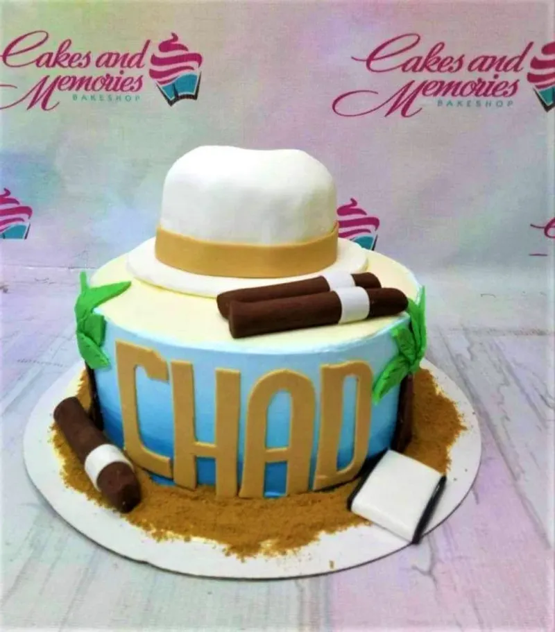 A blue and white fondant cake with a white fedora hat, cigars, and palm trees, featuring the name CHAD in gold letters. A blue and white fondant cake with a white fedora hat, cigars, and palm trees, featuring the name CHAD in gold letters.