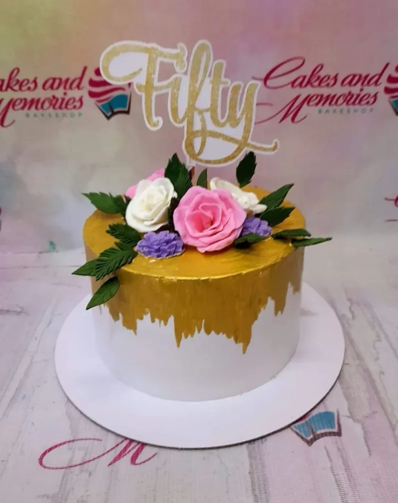 A white and gold 1-tier cake, themed for a Fifty Birthday, featuring a gold glitter 'Fifty' topper and gumpaste roses. A white and gold 1-tier cake, themed for a Fifty Birthday, featuring a gold glitter 'Fifty' topper and gumpaste roses.