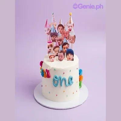 White 1-tier Memory Cake with soft icing, baby face printout toppers with party hats, and colorful piped icing accents White 1-tier Memory Cake with soft icing, baby face printout toppers with party hats, and colorful piped icing accents