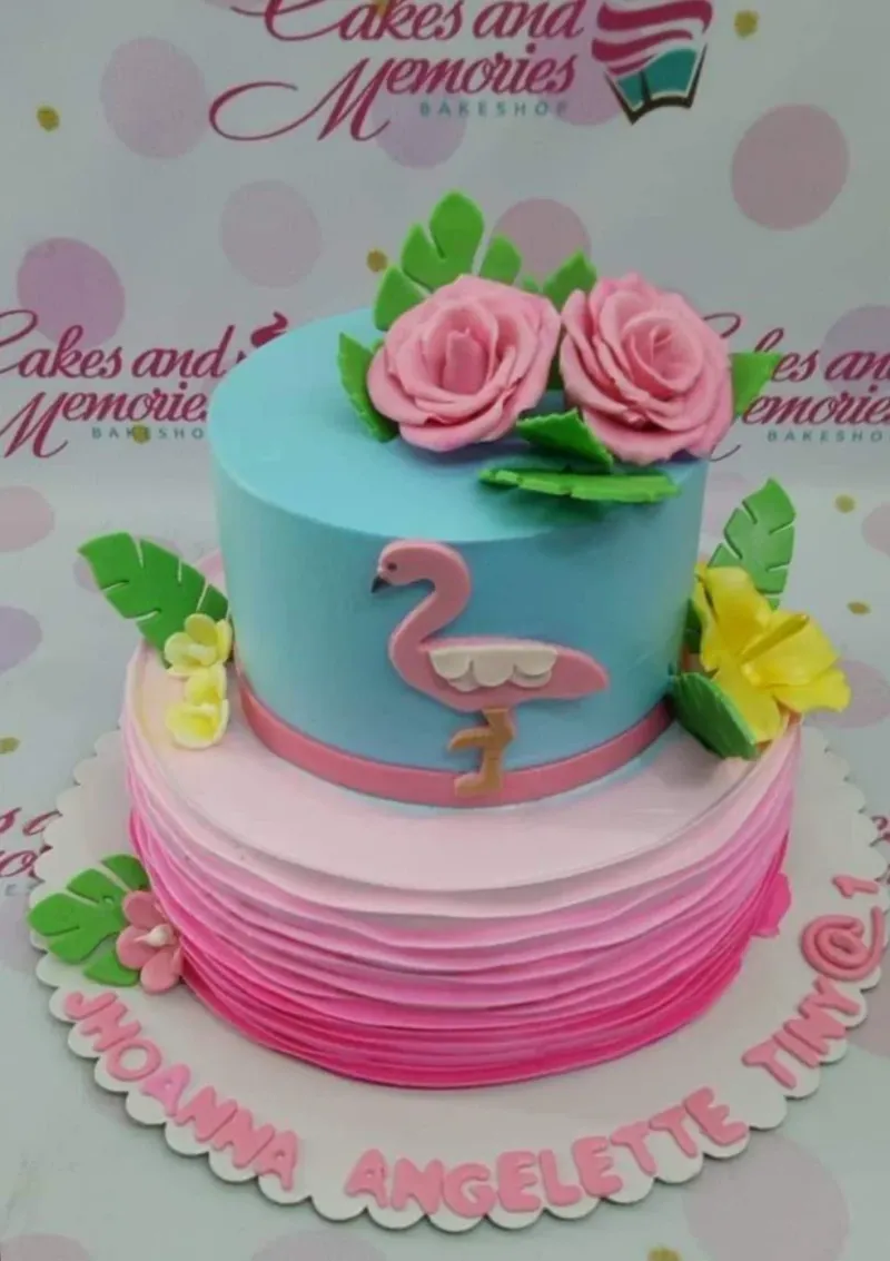 A multicolor Two Tier cake themed Flamingo Tropical, featuring a pink flamingo figure, pink roses, and tropical leaves. A multicolor Two Tier cake themed Flamingo Tropical, featuring a pink flamingo figure, pink roses, and tropical leaves.