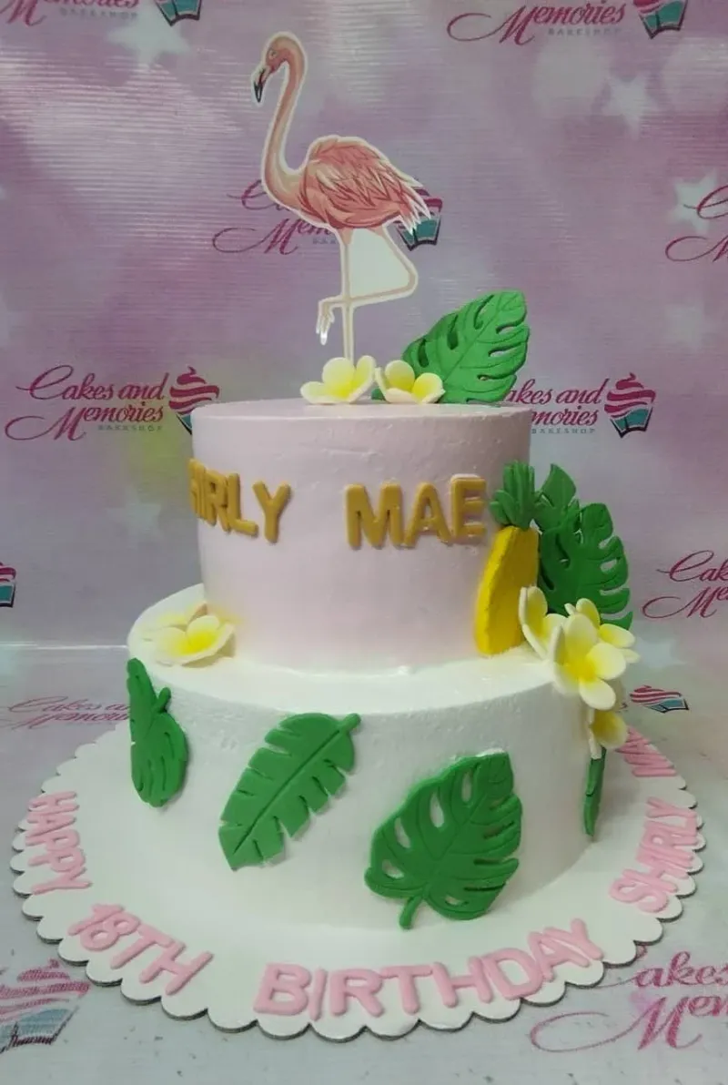 A pink and white 2-tier Flamingo Tropical cake with a flamingo, monstera leaves, and frangipani flowers. A pink and white 2-tier Flamingo Tropical cake with a flamingo, monstera leaves, and frangipani flowers.