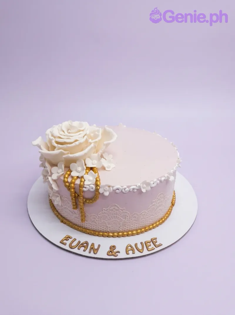 Light pink 1-tier cake with a large white rose, small flowers, gold beads, and white lace. Light pink 1-tier cake with a large white rose, small flowers, gold beads, and white lace.