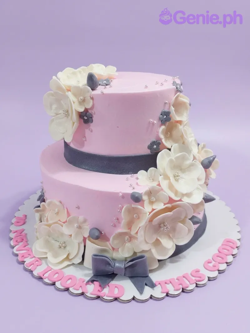 A pink two-tier Floral Birthday cake with white and gray gumpaste flowers, silver dragees, and a gray bow. A pink two-tier Floral Birthday cake with white and gray gumpaste flowers, silver dragees, and a gray bow.