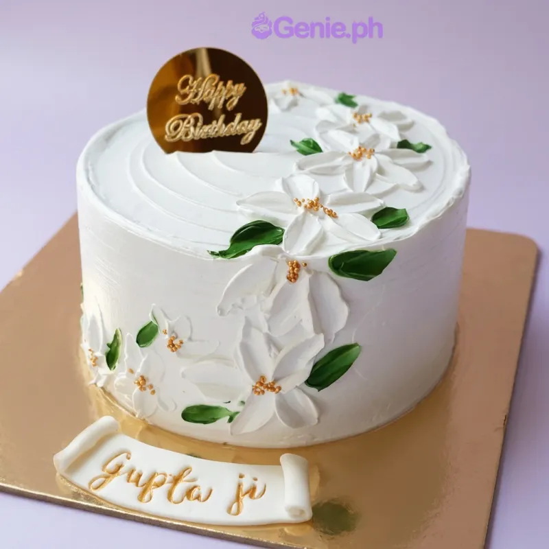 Floral Birthday cake design — 1 layer soft icing cake in white — with gold circular happy birthday topper, white palette knife flowers with green leaves and gold centers, and custom "Happy Birthday" message Floral Birthday cake design — 1 layer soft icing cake in white — with gold circular happy birthday topper, white palette knife flowers with green leaves and gold centers, and custom "Happy Birthday" message