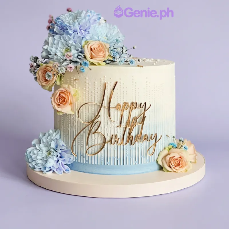 One tier cake with soft white icing, a gold Happy Birthday topper, blue chrysanthemums, peach roses, and white pearl dragees One tier cake with soft white icing, a gold Happy Birthday topper, blue chrysanthemums, peach roses, and white pearl dragees