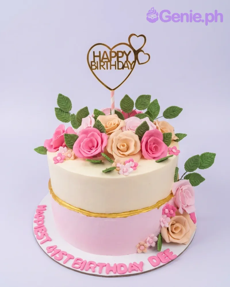A white and pink two-tier floral birthday cake, featuring a gold heart topper, pink and cream roses, and leaves. A white and pink two-tier floral birthday cake, featuring a gold heart topper, pink and cream roses, and leaves.
