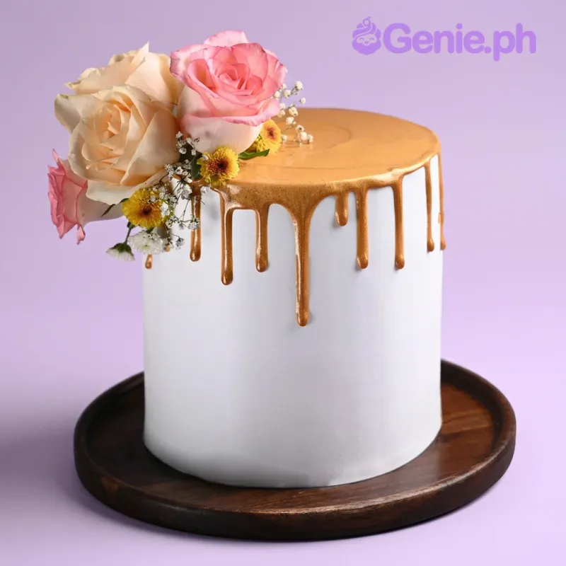 White single-tier cake with a gold drip, topped with a large cluster of fresh pink roses and baby's breath on a wooden board White single-tier cake with a gold drip, topped with a large cluster of fresh pink roses and baby's breath on a wooden board