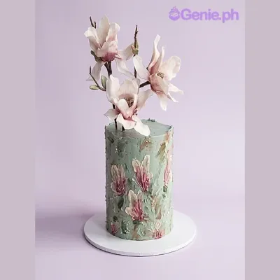 Sage green single-tier cake with large edible magnolia flowers on top and painted floral designs on the side Sage green single-tier cake with large edible magnolia flowers on top and painted floral designs on the side