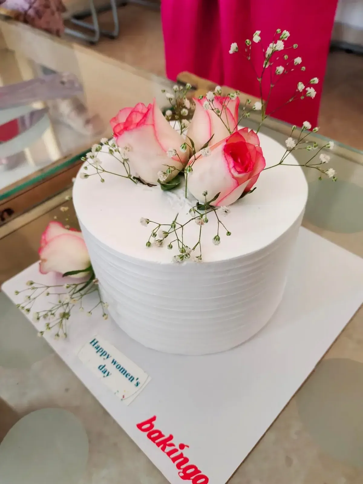 White single-tier cake with soft icing, topped with fresh pink and white roses and baby's breath, and a small message plaque on the base board. White single-tier cake with soft icing, topped with fresh pink and white roses and baby's breath, and a small message plaque on the base board.