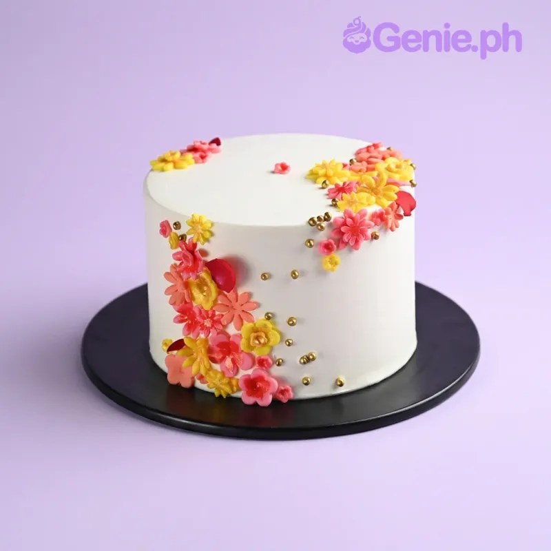 White single-tier cake with smooth soft icing, decorated with colorful pink and yellow edible flowers and gold metallic sprinkles White single-tier cake with smooth soft icing, decorated with colorful pink and yellow edible flowers and gold metallic sprinkles