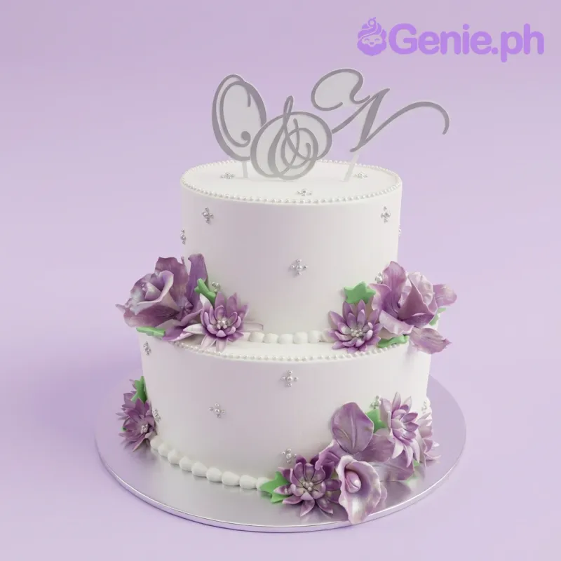 A white 2-tier Floral Monogram cake, featuring monogram initials C and N, purple gumpaste flowers, and silver dragees. A white 2-tier Floral Monogram cake, featuring monogram initials C and N, purple gumpaste flowers, and silver dragees.