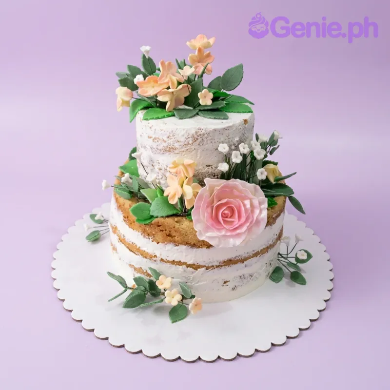 A white two-tier naked cake, featuring a large pink rose, peach gumpaste flowers, and green leaves. A white two-tier naked cake, featuring a large pink rose, peach gumpaste flowers, and green leaves.