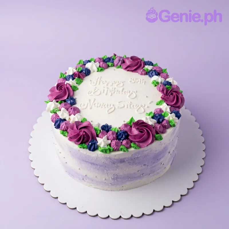 A white 1-tier round cake with purple, pink, green, and silver floral decorations, and a birthday message. A white 1-tier round cake with purple, pink, green, and silver floral decorations, and a birthday message.