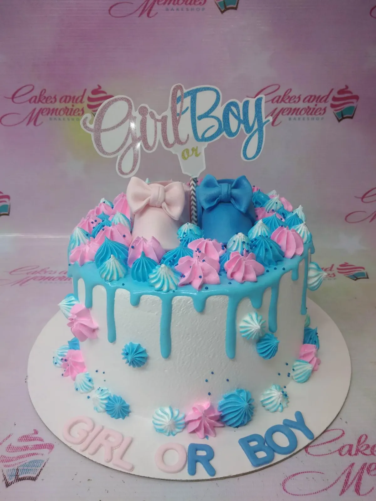 A white 1 Tier gender reveal cake with blue drip, blue and pink icing swirls, a 'Girl or Boy' topper, and pink and blue fondant baby shoes. A white 1 Tier gender reveal cake with blue drip, blue and pink icing swirls, a 'Girl or Boy' topper, and pink and blue fondant baby shoes.